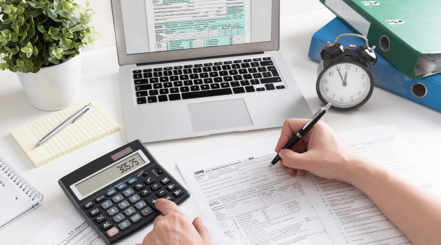 Ręce które rozliczają podatkowo firmę, z tyłu laptop i zegarek