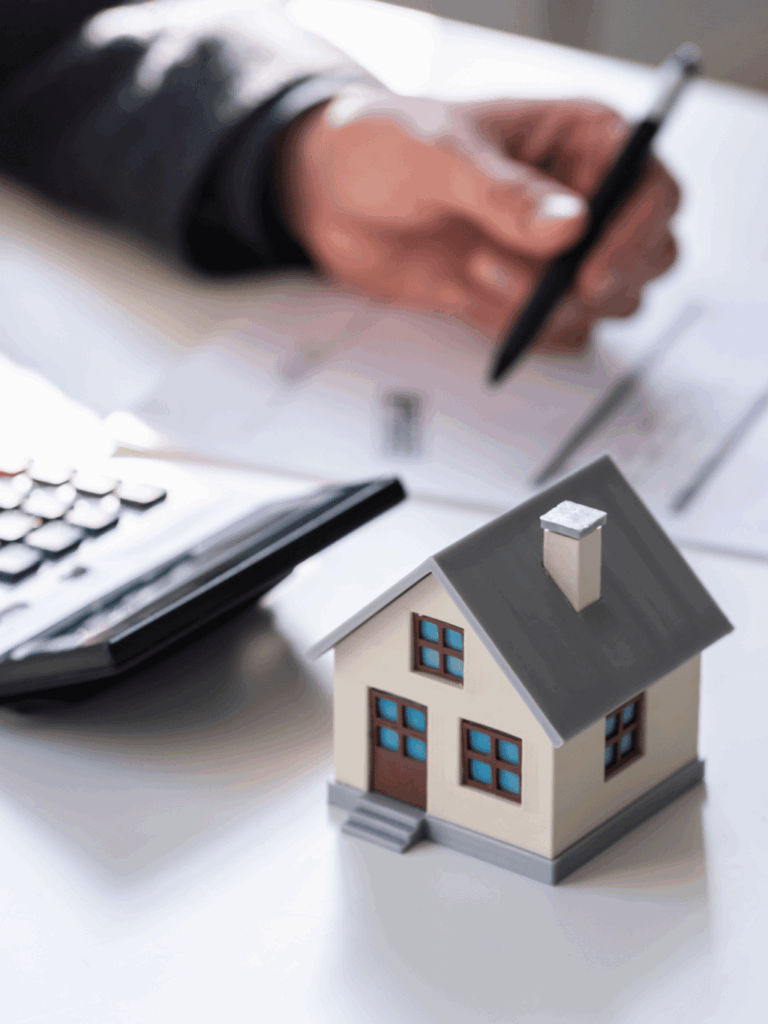 kalkulator umieszczony na biurku z kartką i osobą planującą ochronę majątku rodzinnego, obok kalkulatora stoi mały domek rodzinny