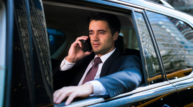 Mężczyzna w garniturze który siedzi w limuzynie i rozmawia przez telefon