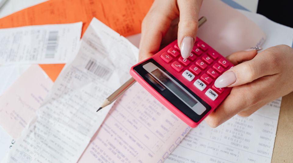 Liczenie kalkulatorem faktury, w tle kilka faktur na biurku